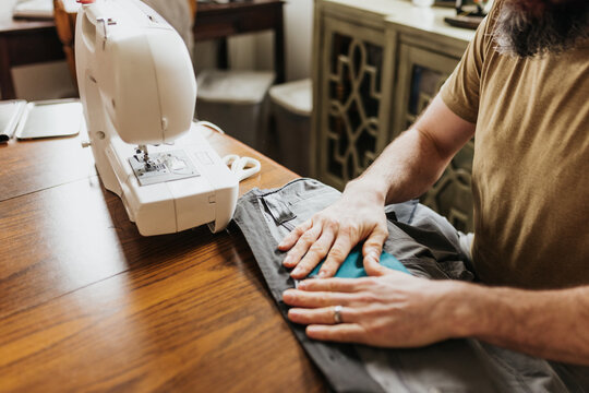 Man sits at kitchen table with sewing machine patching work pants