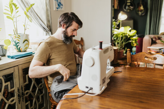 Man sits at kitchen table with sewing machine patching work pants