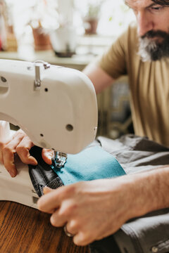 Man sits at kitchen table with sewing machine patching work pants