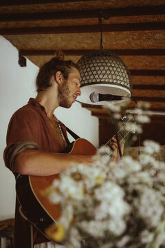Young man musician plays the guitar and sings into a microphone.