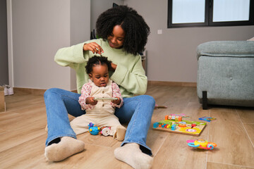 Cuban mother comb her toddler daughter hair while she use the phone.