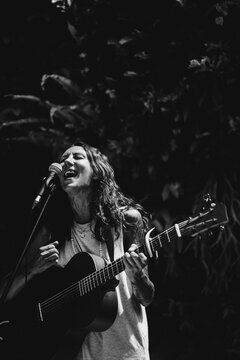 Young woman singer, sings into a microphone and plays the guitar.