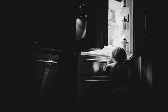 Child peers into fridge's glow in a quiet home