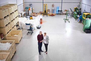 Obraz premium Factory, warehouse and business people with tablet for logistics training, management and communication. Mature man, woman and discussion with tech for teamwork, planning or conversation from above