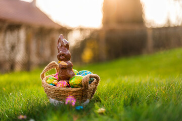 Easter eggs in basket in grass. Colorful decorated easter eggs in wicker basket. Traditional egg hunt for spring holidays. Morning magical light - obrazy, fototapety, plakaty