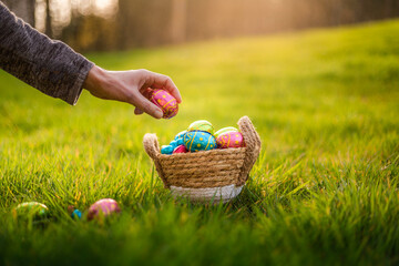 Easter eggs in basket in grass. Colorful decorated easter eggs in wicker basket. Traditional egg hunt for spring holidays. Morning magical light - Powered by Adobe