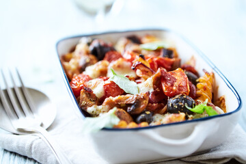 Baked pasta with cherry tomatoes, olives and mozzarella cheese. Bright wooden background. Close up.	
