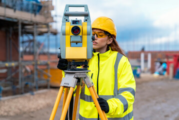 Female site engineer surveyor working with theodolite total station EDM equipment on a building construction site outdoors - obrazy, fototapety, plakaty