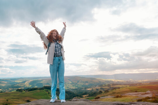 amazing redhead woman with  backpack raising her hands, reaching the destination and enjoying mountains landscape on the top of mountainon cloudy day. Enjoy hiking and exploring new places concept