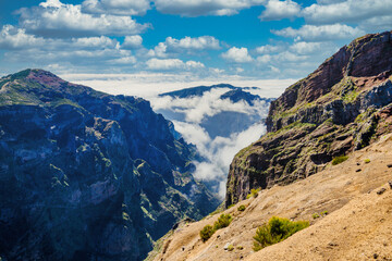 Fototapeta na wymiar The picturesque stone trail PR 1 in Madeira. The route leads through rocky terrain, surrounded by lush greenery, under a blue sky with white clouds, creating a harmonious image of the island's natural