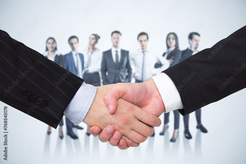 Poster close up of two men shaking hands with their diverse blurry colleagues in the background. concept of