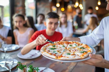 Fotobehang waiter serving a pizza to a table of young adults at a pizzeria © studioworkstock