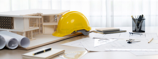 Yellow safety helmet was placed with architectural equipment, house model and blueprint scatter...