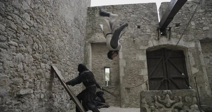 Hooded man chasing backflipping knight in slow motion - ancient castle