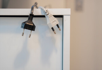 Black and white electric plugs hanging from the sideboard cabinet at office.