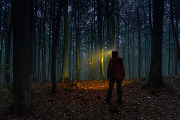Girl tourist with a large backpack in the night forest. A traveler lights the way with a headlamp