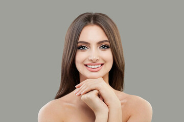 Cute model woman with fresh clear skin smiling on gray background. Facial treatment, skincare and cosmetology concept
