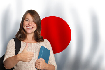 Positive woman student showing thumb up against Japanese flag background. Travel, education and learn language in Japan concept - 768560181