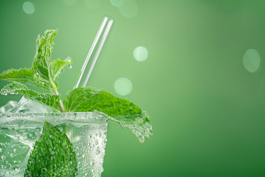 Close-up image of a chilled mint julep glass with condensation droplets, mint sprigs, and a straw, set against a cool, green, gradient background with empty space for text 