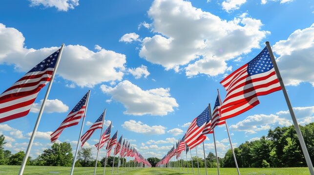 Row of American flags waving against a blue sky with clouds.
