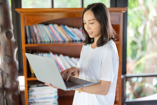 half body photo Asian female student Study online, use your laptop, work on the balcony, and have a library and extensive collection of books for research on comfortable and relaxing days.