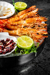 Grilled shrimps with fresh lime, herbs, and spices on a dark textured surface, showcasing a delightful meal presentation