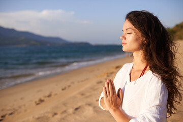Prayer hands, woman and meditation on beach with mindfulness, eyes closed and zen with fresh air for calm outdoor. Ocean, breeze and travel with yoga for health, peace of mind and holistic healing