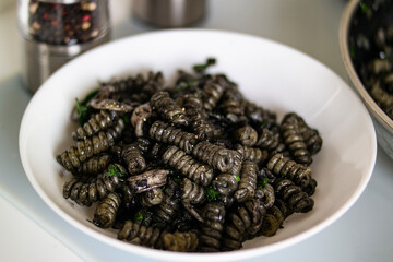 Black pasta dish garnished with white larva on the table