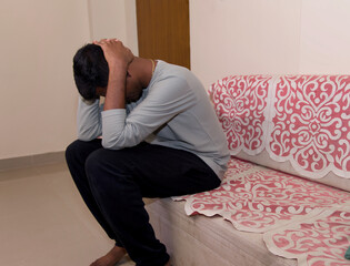 Depressed young man sitting on sofa in living room at home