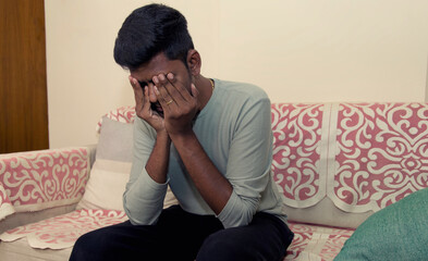 indian man sitting on sofa and covering his face with his hands