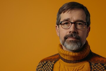 Portrait of mature man with grey beard wearing eyeglasses and sweater on yellow background