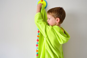 young boy hanging up a neon green bathrobe on a colorful hook - obrazy, fototapety, plakaty