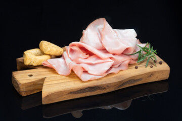 Slices of mortadella on wooden cutting board with sprig of rosemary, black pepper and salty...