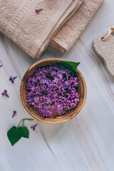 Spa and wellness composition with perfumed lilac flowers water in wooden bowl and terry towels on marble background, aromatherapy, top view, flat lay.