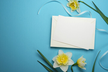 Flat lay easter frame with daffodils and blank white greeting card on a blue background. Top view, copy space. Mock up. 