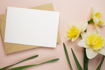 Blank white greeting card and envelope with daffodil flowers on light background. Top view, flat lay. Mock up. Easter background.
