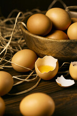 Raw eggs on a brown woody background  with one broke egg on a straw pillow, brown bowl with eggs inside