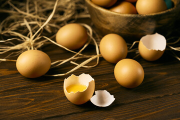 Raw eggs on a brown woody background  with one broke egg on a straw pillow, brown bowl with eggs inside