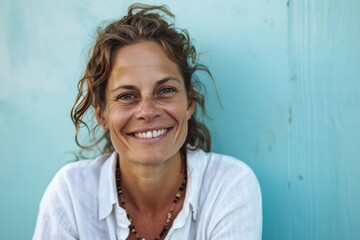 Portrait of a smiling middle-aged woman against a blue wall - obrazy, fototapety, plakaty