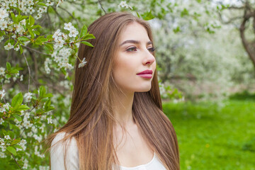 Beauty portrait of fashion model with long brown hair and natural makeup against floral background outdoor - 768592587