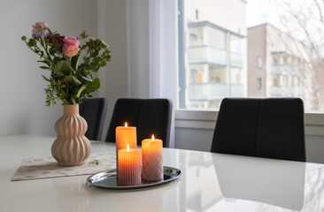 Three pink candles and a bouquet of flowers in a vase on the table. Photo