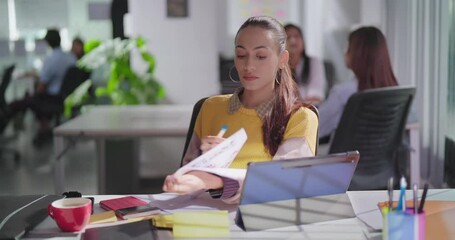 Indian Asian Hindu gen z young adult busy girl lady sitting chair indoor job office do work day task use tablet touch pad audit female worker hold paper bank data pay loan tax check online bill cost