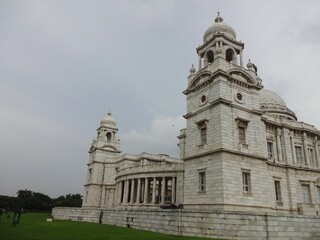 Obraz premium The grand Victoria Memorial Hall stands under a dramatic cloud-filled sky, showing off its exquisite colonial architecture with its towering domes and intricate stonework.