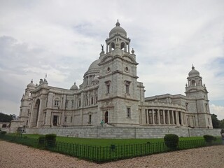 Obraz premium The grand Victoria Memorial Hall stands under a dramatic cloud-filled sky, showing off its exquisite colonial architecture with its towering domes and intricate stonework.