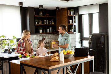 Family chatting and preparing food around a bustling kitchen counter filled with fresh ingredients and cooking utensils - obrazy, fototapety, plakaty