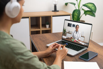 Patient with headphones engaged in a telemedicine session with a doctor on a laptop.