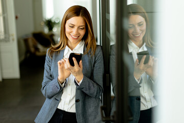 Smiling Businesswoman in Modern Office Holding Smartphone Enjoying a Successful Work Day