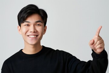asian american male person with toothy smile on face pointing with index finger on empty space over white background. Handsome young guy indicating place for advertising text in studio