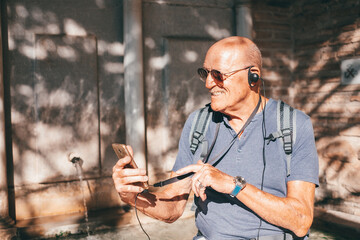 Happy senior bald man visiting Alhambra in Granada in a sunny day listening to informations via audio guide, Elderly man enjoying vacation and retirement traveling in Europe