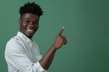 African american male person with toothy smile on face pointing with index finger on empty space over green background. Handsome young guy indicating place for advertising text in studio